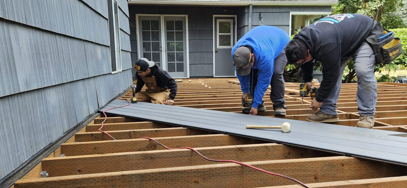 Three crew members kneeling on new joists, fastening the first composite boards