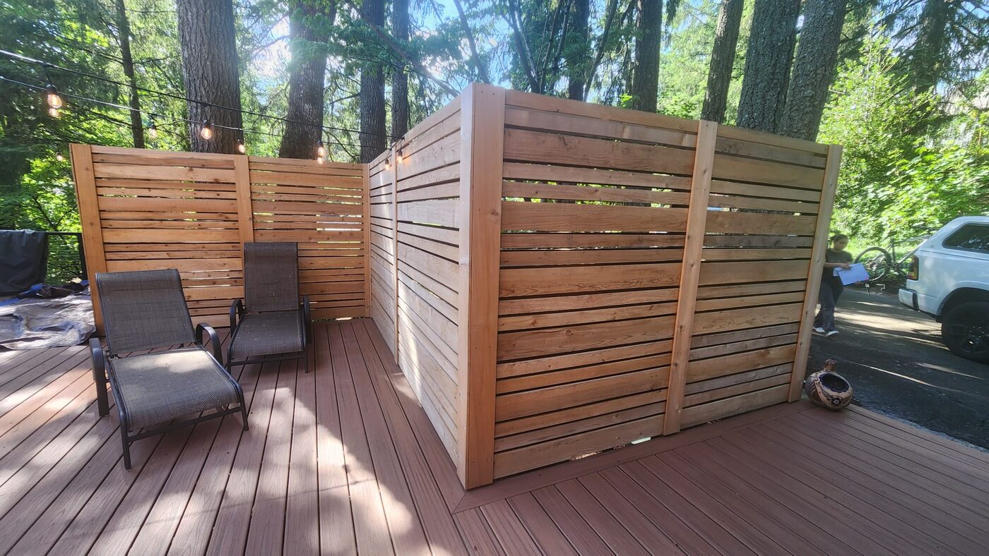 A cedar privacy wall forming a deck nook with lounge chairs and string lights