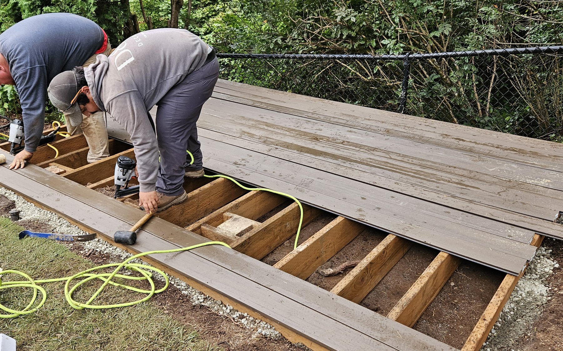 Two crew members laying new deck boards over an existing frame, the old boards stripped and stacked beside them